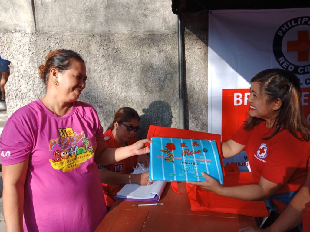 Philippine Red Cross volunteers help distribute the blankets to the affected fire victims.